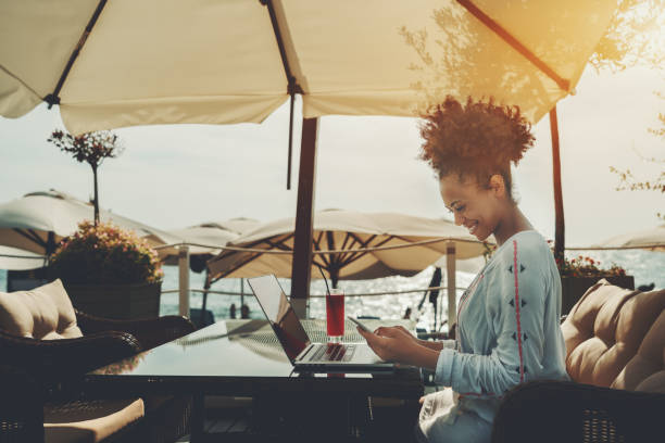 Woman working on a laptop at a sunlit oceanfront terrace